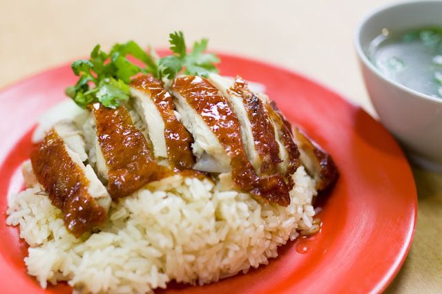 a plate of sumptious Hainanese roasted chicken rice, the rice was steamed in chicken stock, served on a red plate, topped off with slices of roasted chicken breast with soy-sauce marinated brown skin, and topped off with a sprig of coriander leaves.