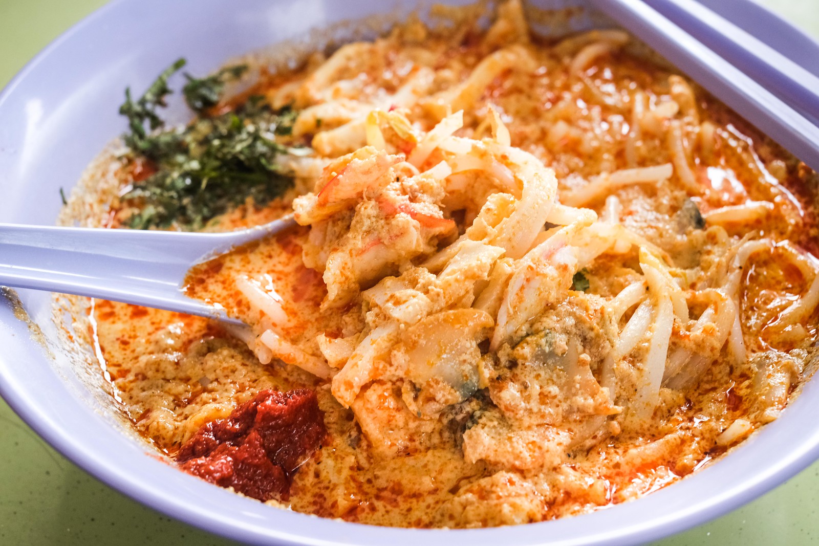 a sumptious bowl of laksa. a bowl of spicy laksa rempah broth with coconut milk, hosting a ballad of rice vermicelli, with a myriad of toppings including fish cakes, cockles, bean sprouts, prawns and laksa leaves.